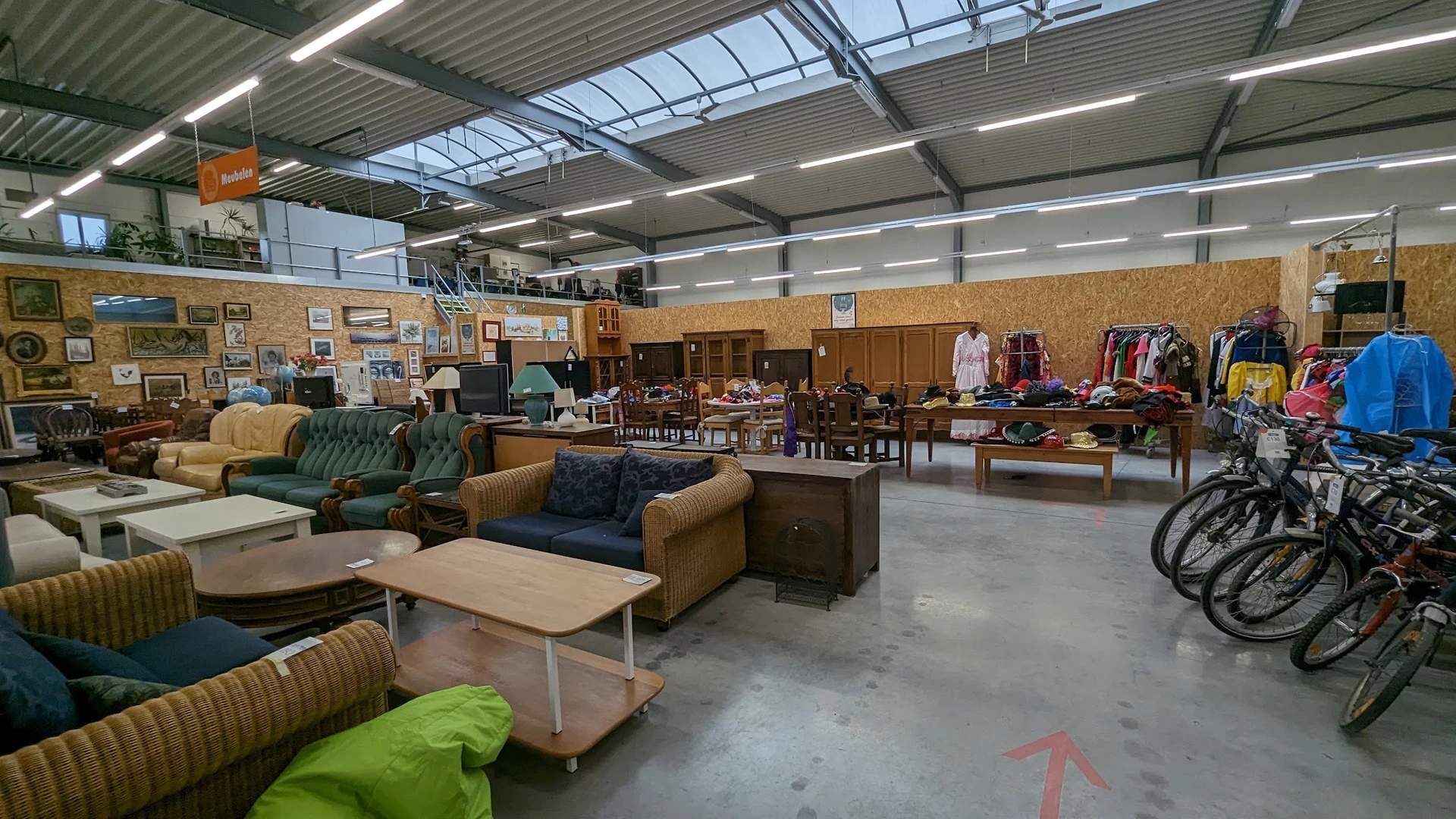 Ruim magazijn met tweedehands meubels, kleding en huishoudspullen uitgestald op verschillende locaties