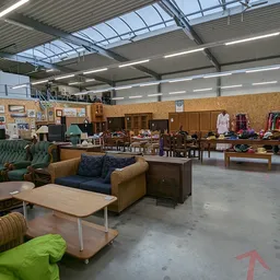 Ruim magazijn met tweedehands meubels, kleding en huishoudspullen uitgestald op verschillende locaties
