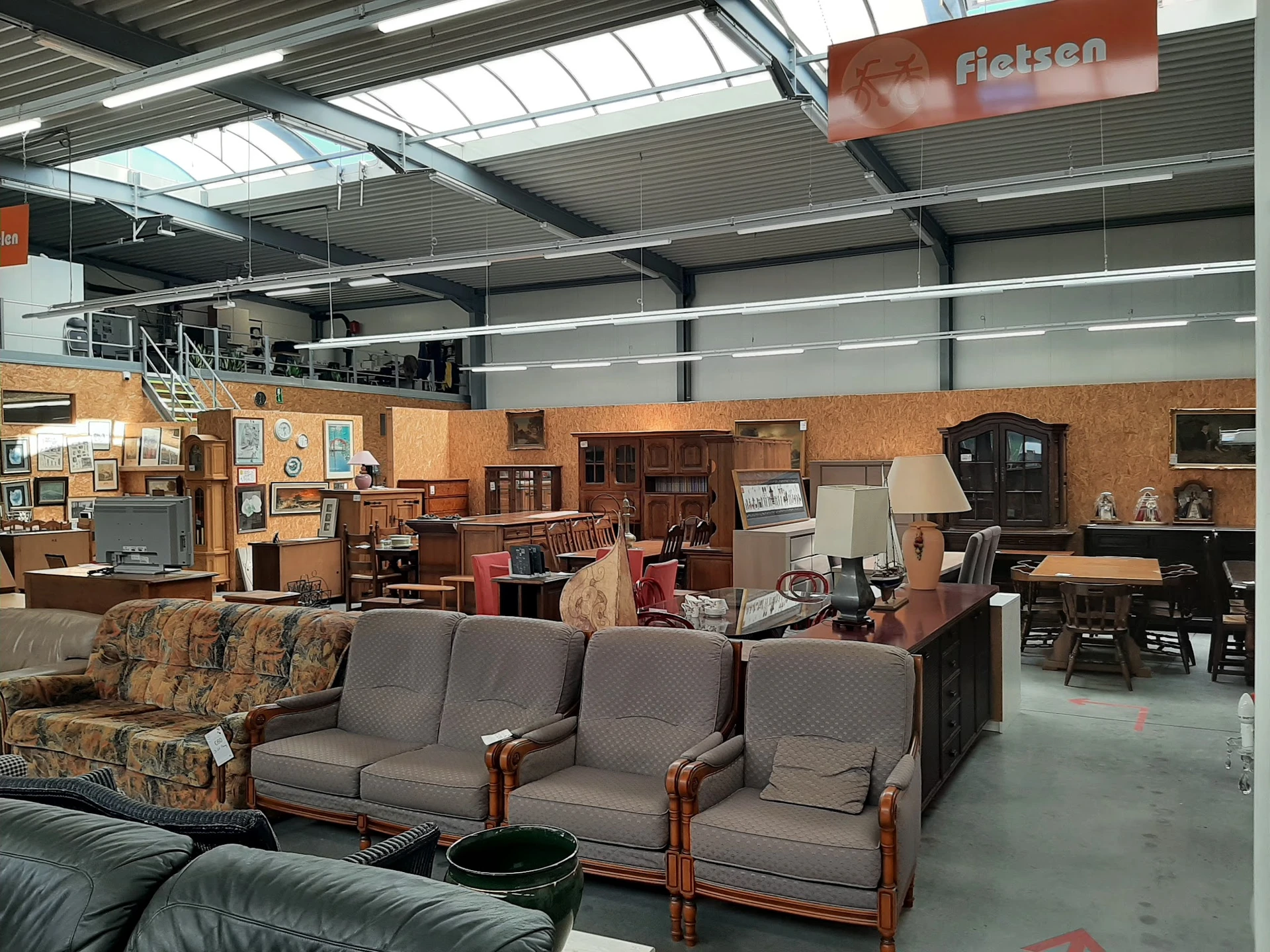 Winkelvloer met meubels: banken en stoelen met houten frames, houten kasten en tafels tegen een bakstenen wand