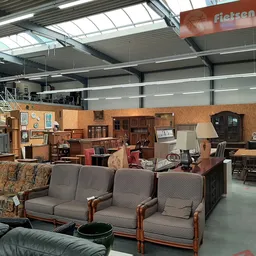 Winkelvloer met meubels: banken en stoelen met houten frames, houten kasten en tafels tegen een bakstenen wand