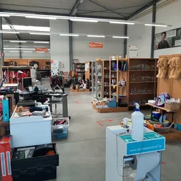 Ruime winkelruimte met diverse stellingen, kleding, boeken en huishoudartikelen verspreid over de vloer