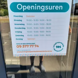 Openingsuren op een wit bord met teal header, geplakt op een glazen deur