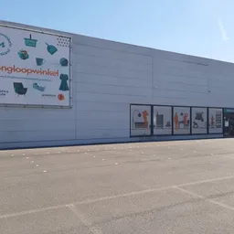 Grijze gevel van kringloopwinkel met logo en uitstalbakken, parkeerterrein ervoor