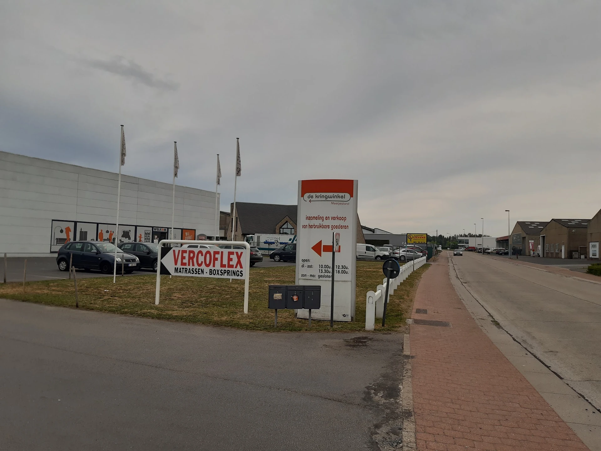 Voorgevel van kringloopwinkel met Vercoflex-bord, parkeerplaats en straatje ernaast