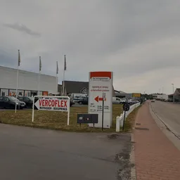Voorgevel van kringloopwinkel met Vercoflex-bord, parkeerplaats en straatje ernaast