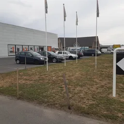 Parkeerterrein met auto's en vlaggen voor een grijze winkelgebouw