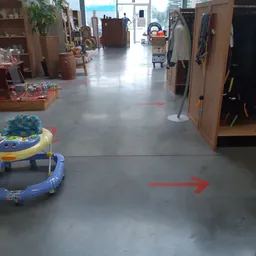 Winkelvloer met rode pijlen als richtlijnen, babyspeelgoed links, kasten en rekken met spullen langs de zijkanten
