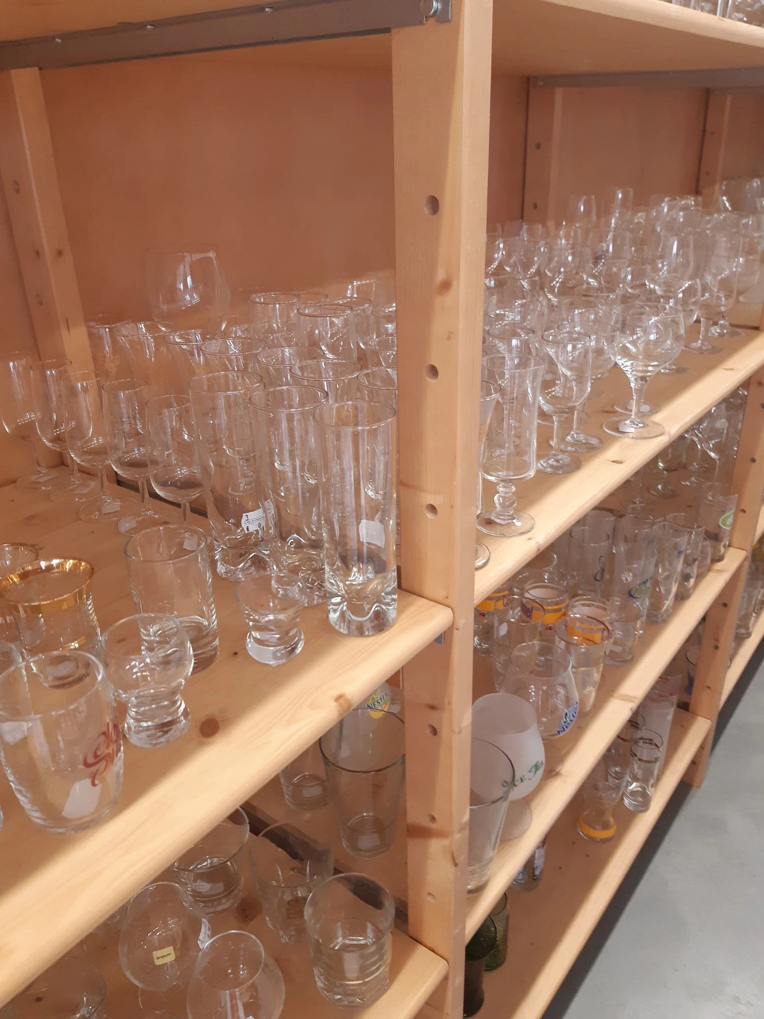 Houten stellingen gevuld met diverse glazen in verschillende vormen en maten