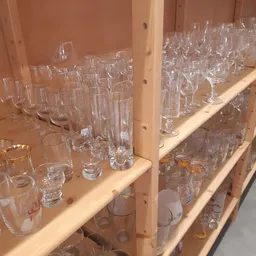 Houten stellingen gevuld met diverse glazen in verschillende vormen en maten