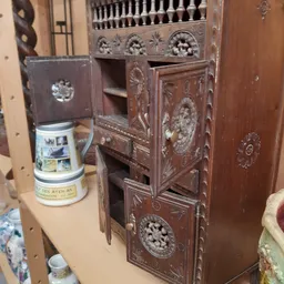 Houten kastje met decoratieve snijwerk en een keramische pot ernaast