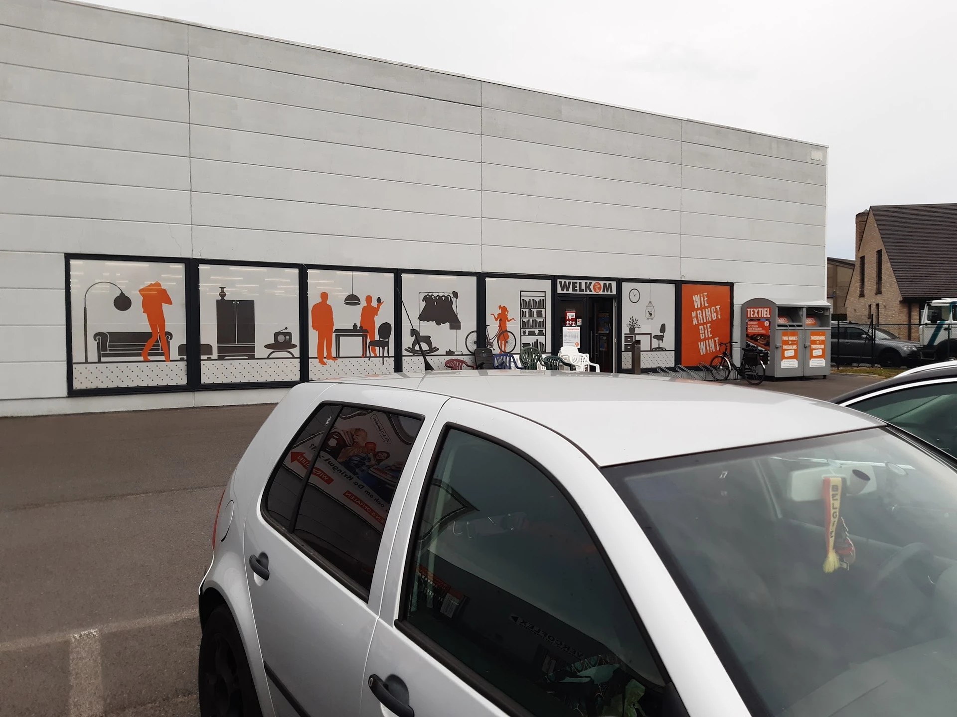 Grijze gevel van kringloopwinkel met etalagevensters met oranje en zwarte decoratie en merchandise