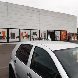 Grijze gevel van kringloopwinkel met etalagevensters met oranje en zwarte decoratie en merchandise