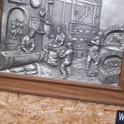 Zilverkleurig reliëfwerk in houten lijst toont een bakerijtafereel met figuren