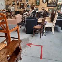 Winkelvloer met diverse meubels: houten stoelen, fauteuils, tafels en kasten met framed afbeeldingen op achtergrond