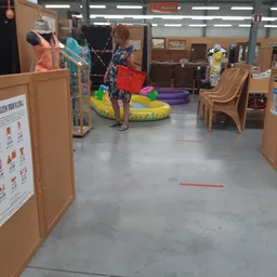 Winkelvloer met houten kastjes, gele en groene zitzakken, paarse speelkubus en rode markeringen op de grond