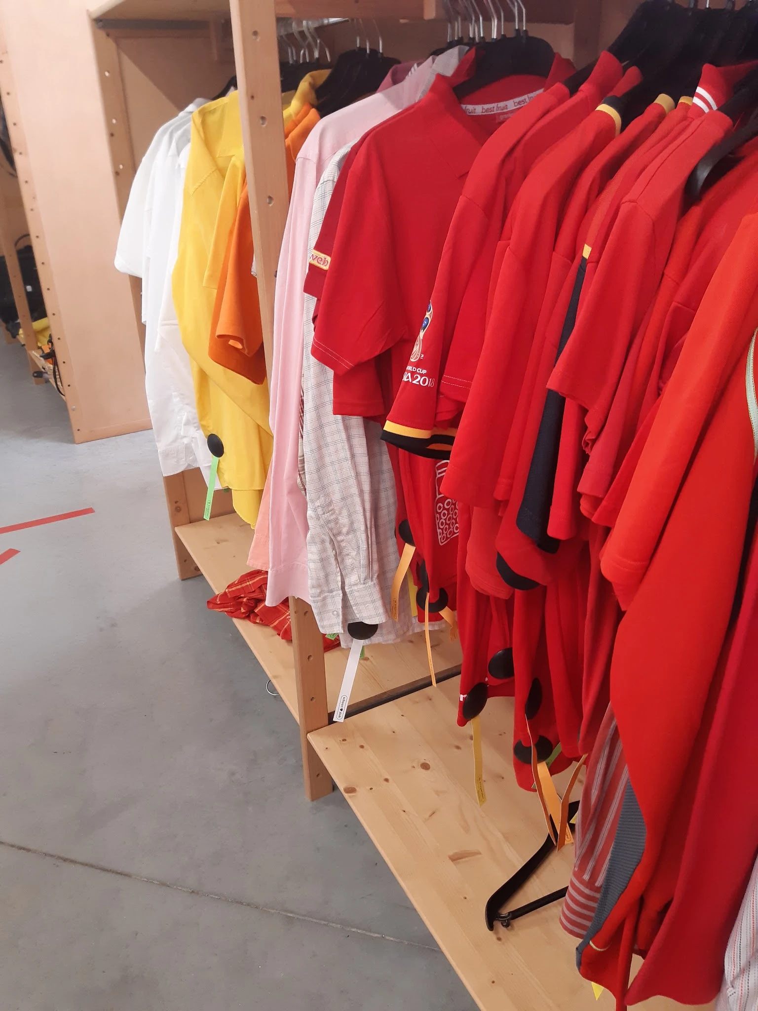 Rekken met tweedehands kleding in verschillende kleuren: rood, geel, wit en roze