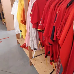 Rekken met tweedehands kleding in verschillende kleuren: rood, geel, wit en roze