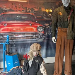 Vintage kleding en accessoires uitgestald voor een grote muurschildering met een klassieke rode auto en modepop