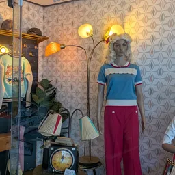 Etalage met vintage kleding op een mannequin en vintage lampen tegen behangde wand