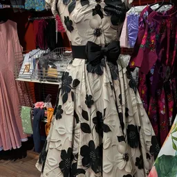 Vintage jurk met zwart-wit bloemenprint en zwarte strik op etalagepop, omgeven door andere kleding op rekken.