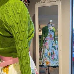 Vintage kleding op hangers: felgroene gebreide vest en kleurrijke bloemenprint jurk