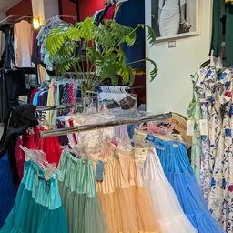 Rekken met kleurige vintage jurken en rokken in verschillende tinten, met hangers en winkelinterieur op de achtergrond