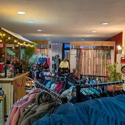 Winkelvloer met kledingrekken, vintage decoraties en decoratief houten huisje onder plafondverlichting