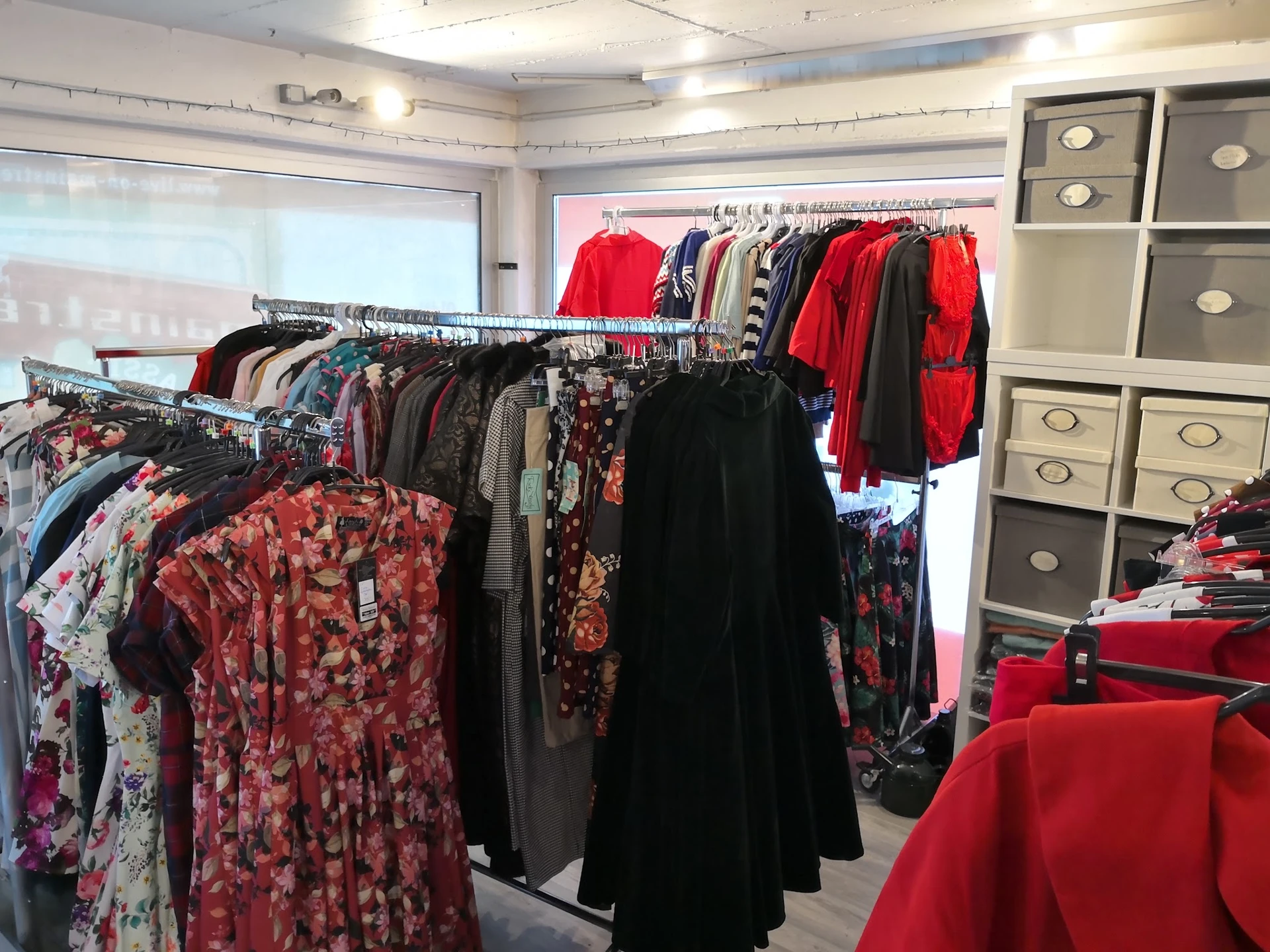Rekken met tweedehands dameskleding in diverse kleuren en patronen, vooral rode en bloemenprint items