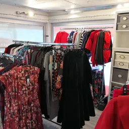 Rekken met tweedehands dameskleding in diverse kleuren en patronen, vooral rode en bloemenprint items