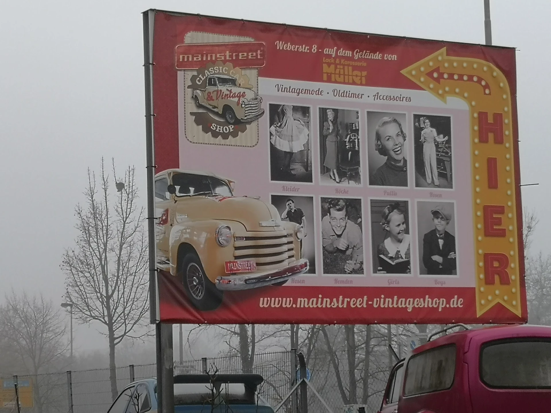 Groot reclamebord van vintage winkel met oude auto en zwart-witfoto's, langs straat met kale boom