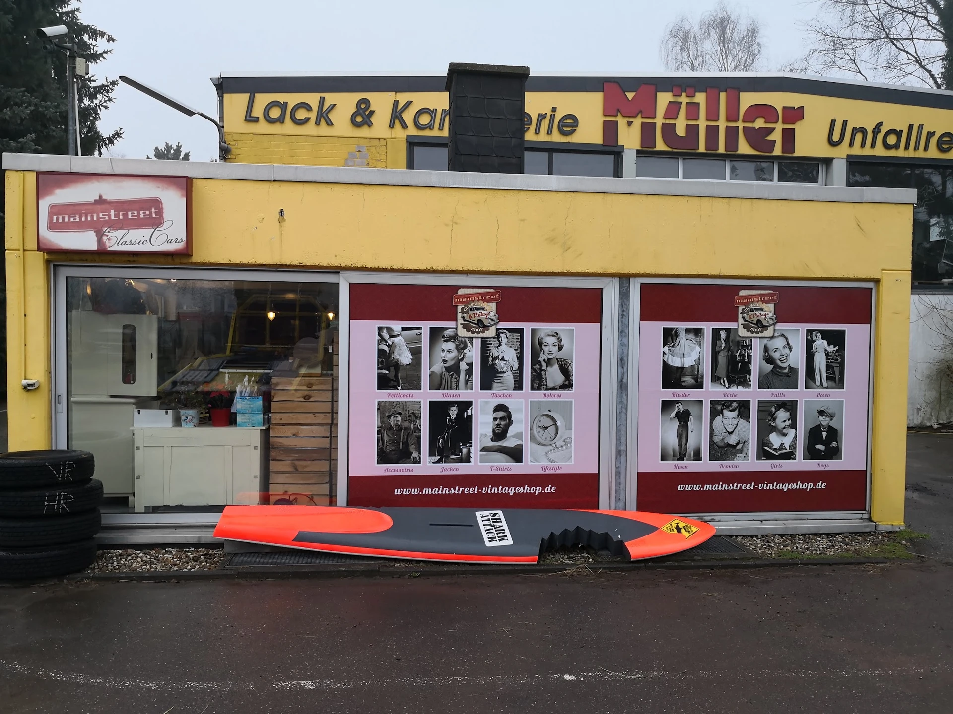 Gele winkelgevel met zwart dak, rode vintage foto's in etalageruiten, rood surfboard ervoor