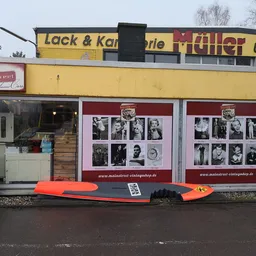 Gele winkelgevel met zwart dak, rode vintage foto's in etalageruiten, rood surfboard ervoor