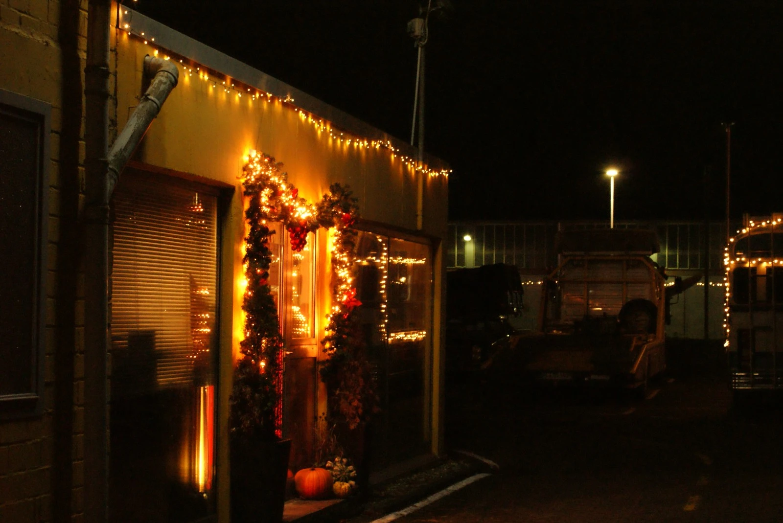 Winkelgevel 's nachts verlicht met gele kerstverlichting en rode kerstkransen om de ingang