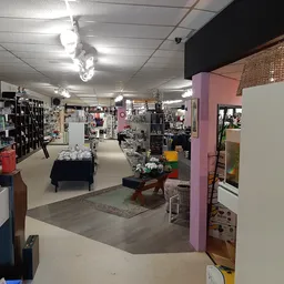 Overzicht van de winkelvloer met stellingen, rekken met tweedehands spullen, paarse decoratieve kolom en diverse afdelingen