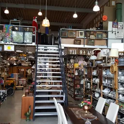 Overzicht van de kringloopwinkel met stellingen vol spullen, trappen in het midden en hangende lampen