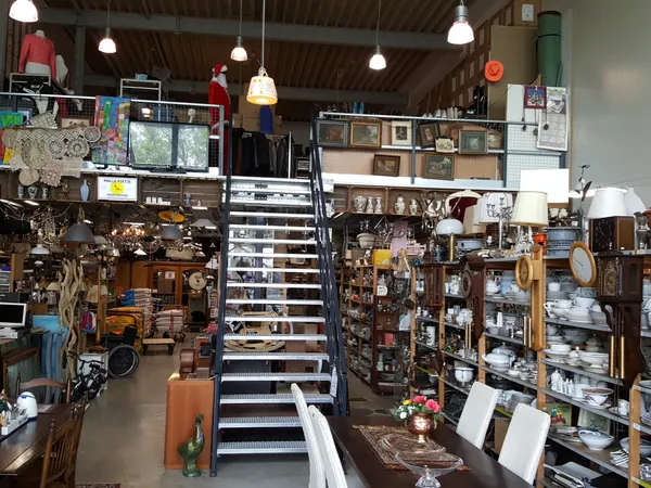 Overzicht van kringloopwinkel met trappen, stellingen vol spullen, lampen en diverse gebruiksartikelen