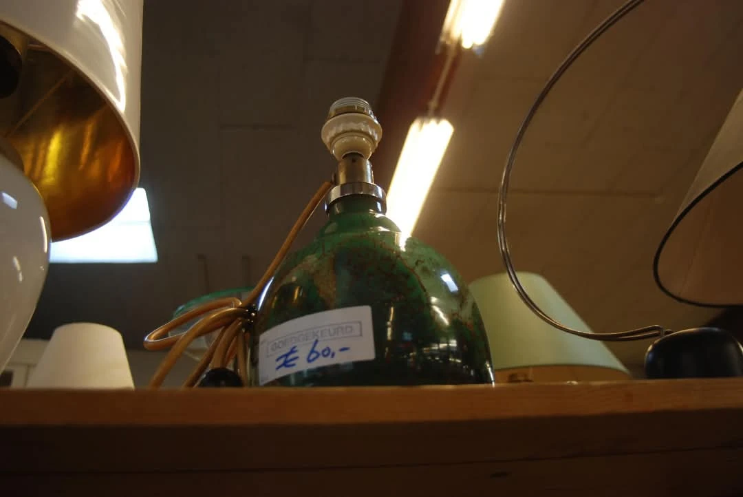 Groene glazen fles met dop en label op een houten plank onder spotlights