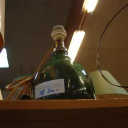 Groene glazen fles met dop en label op een houten plank onder spotlights