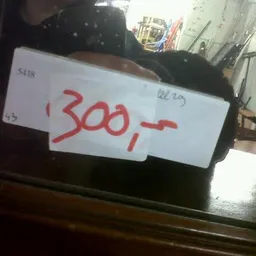 Handgeschreven prijskaartje met '300,-' op wit papier op zwart artikel