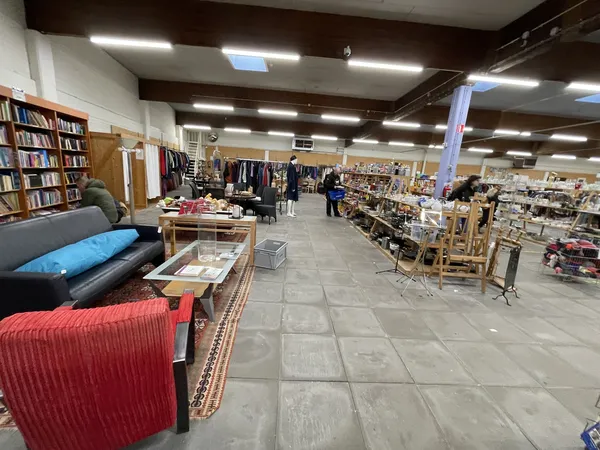 Binnenaanzicht van kringloopwinkel met boekenkasten, meubels, kleding op hangers en diverse spullen uitgestald