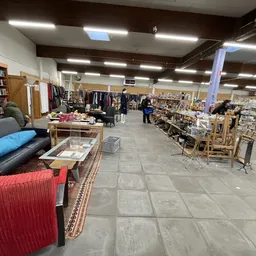 Overzicht van kringloopwinkel met boekenkasten, kleding aan hangers, meubels en diverse goederen uitgestald