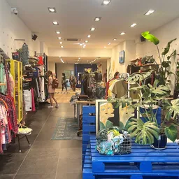 Winkelinterieur met kledingrekken aan beide zijden, blauwe pallets met planten in het midden, goed verlicht