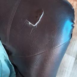 Close-up van een bruin leren kledingstuk met slijtage en een witte naad