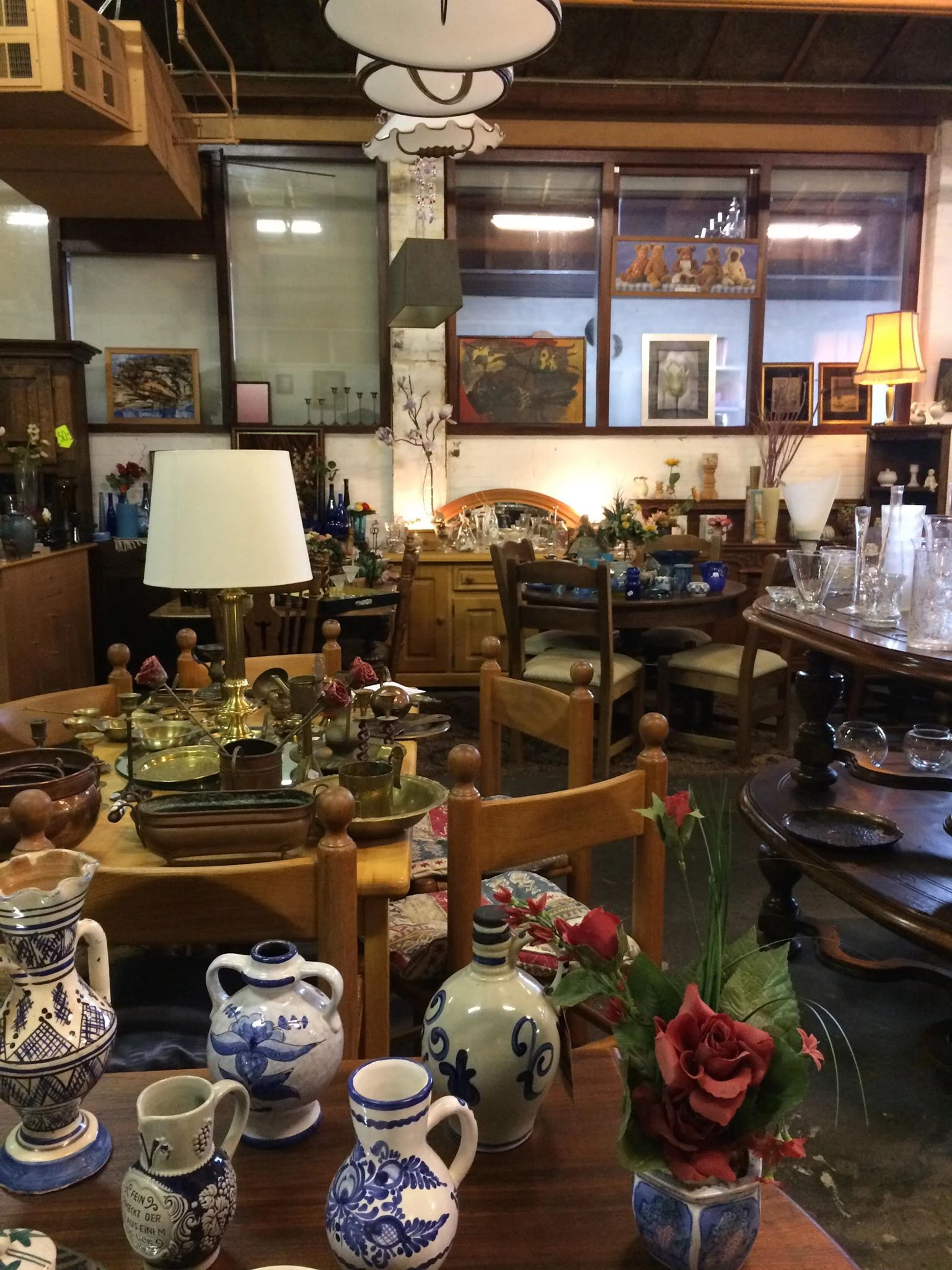 Interieur van kringloopwinkel met houten meubels, tafels met servies, lampen en decoratieve items, wandkasten vol voorwerpen 