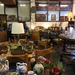 Interieur van kringloopwinkel met houten meubels, tafels met servies, lampen en decoratieve items, wandkasten vol voorwerpen 