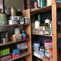 Houten stellingen met diverse gebruikte huishoudartikelen, blikken, dozen en keukenbenodigdheden