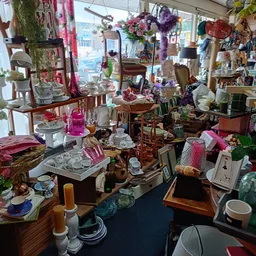 Drukke winkelinterieur met diverse meubels, serviesgoed, lampen en decoratieve spullen op stellingen en tafels