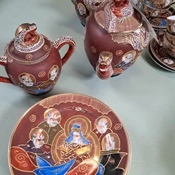 Rode porseleinen theepotten en bord met religieuze afbeeldingen en gouden decoratie