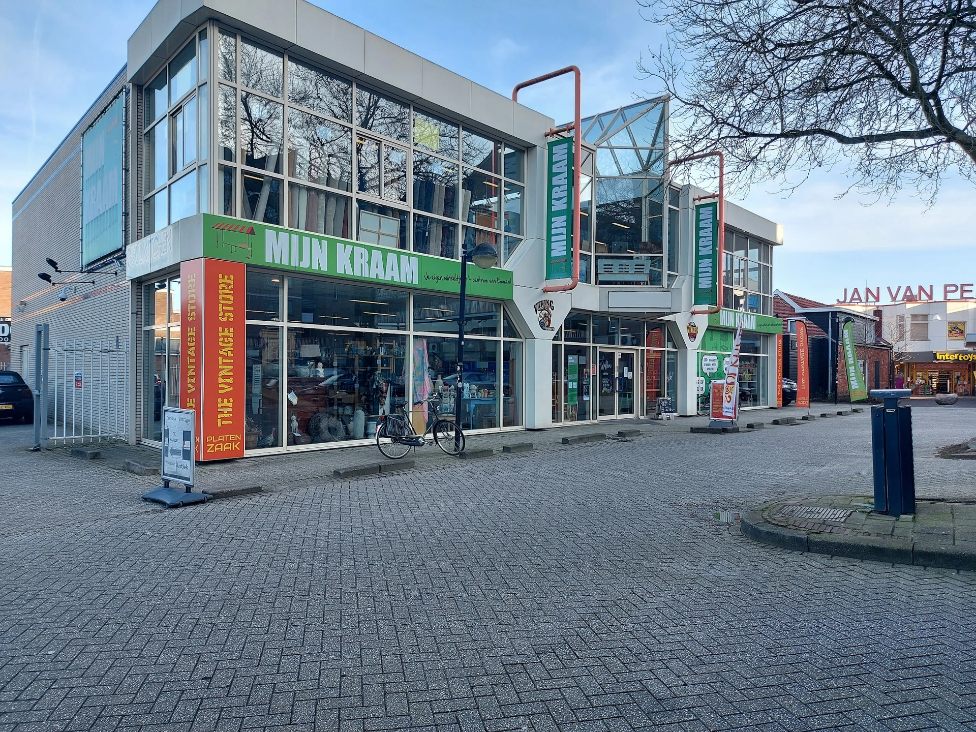 Gevel van kringloopwinkel Mijn Kraam met groene letters, winkelramen en glazen bovenbouw aan Noorder Passage in Emmen