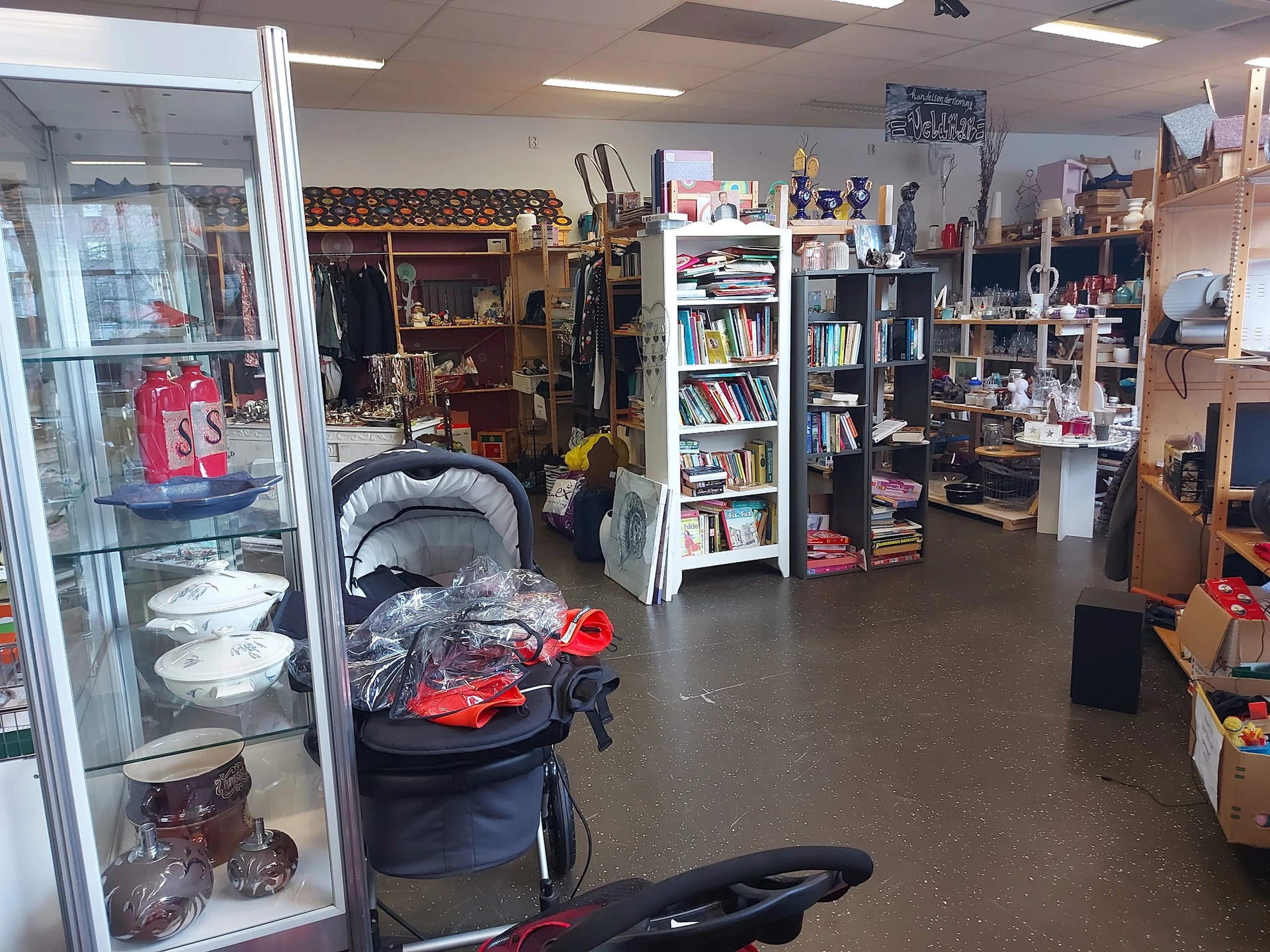 Winkelvloer van kringloopwinkel met stellingen, boeken, kinderwagen, huishoudspullen en diverse tweedehands goederen
